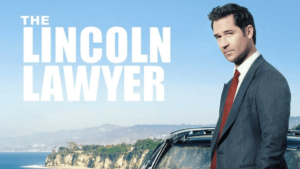 A man in a suit leans against a car overlooking the California coast