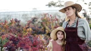 A young girl and older woman stand amid hundreds of wildflowers wearing large sun hats