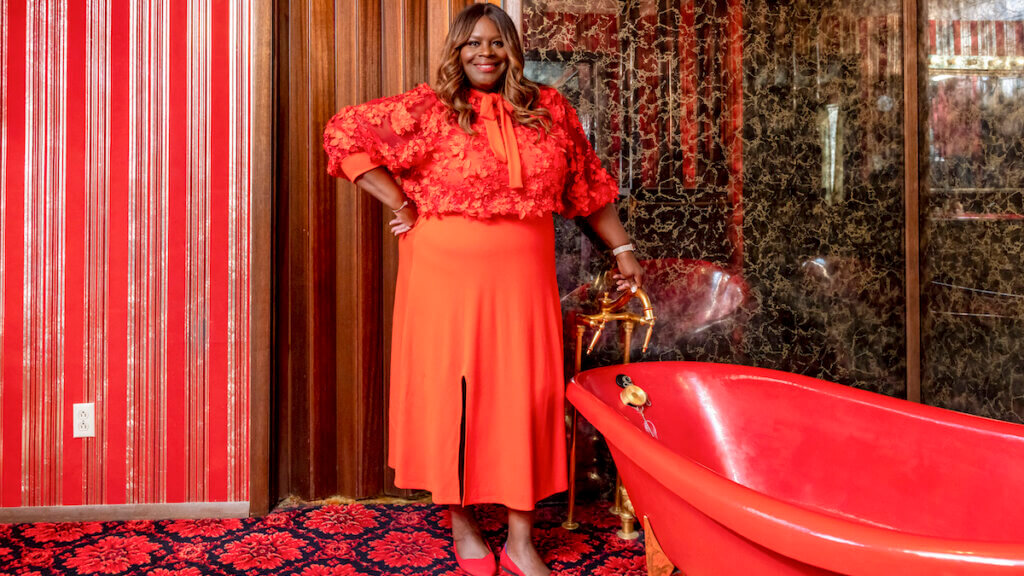 Actor and comedian Retta in a red outfit in an ugly red bathroom