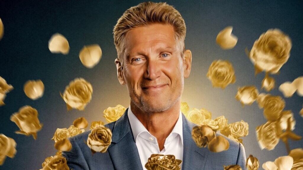 An older gentleman smiles at the camera surrounded by falling gold rose petals