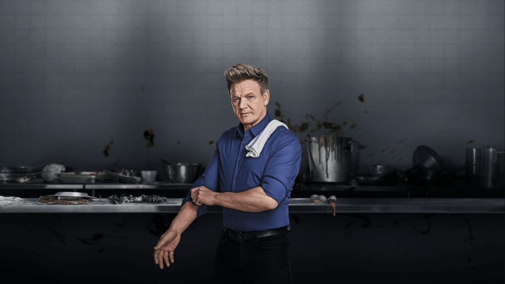 Chef Gordon Ramsay rolling up his sleeves in front of a messy kitchen counter