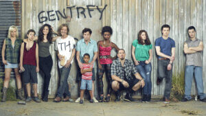 A large family and extended family of tough looking characters along a fence spray painted with "gentrify this"
