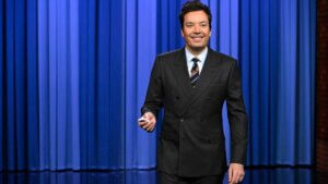 Host Jimmy Fallon in front of a blue stage curtain