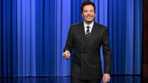 Host Jimmy Fallon in front of a blue stage curtain
